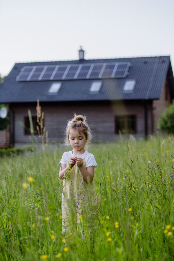 Portrait of a little girl in front of family house with solar panels, concept of sustainable lifestyle and renewable resources.