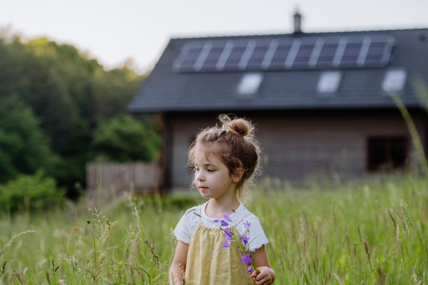 Portrait of a little girl in front of family house with solar panels, concept of sustainable lifestyle and renewable resources.