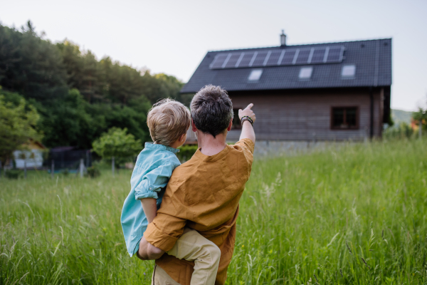 Rear view of father and his son looking at their house with solar panels on a roof.