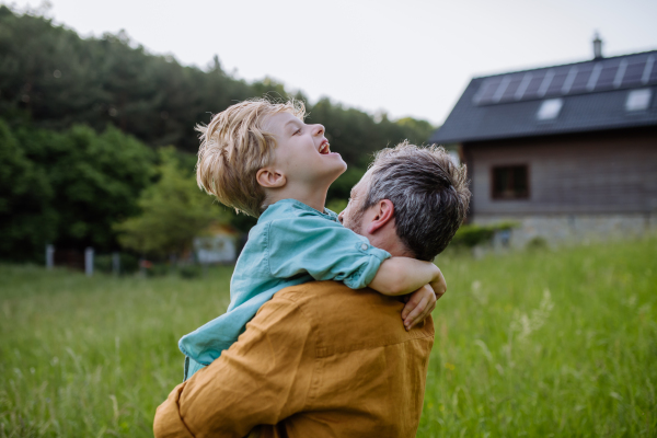 Rear view of father and his son looking at their house with solar panels on a roof.