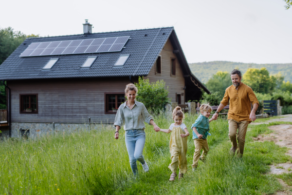 Happy family in front of their house with a solar panels on the roof.