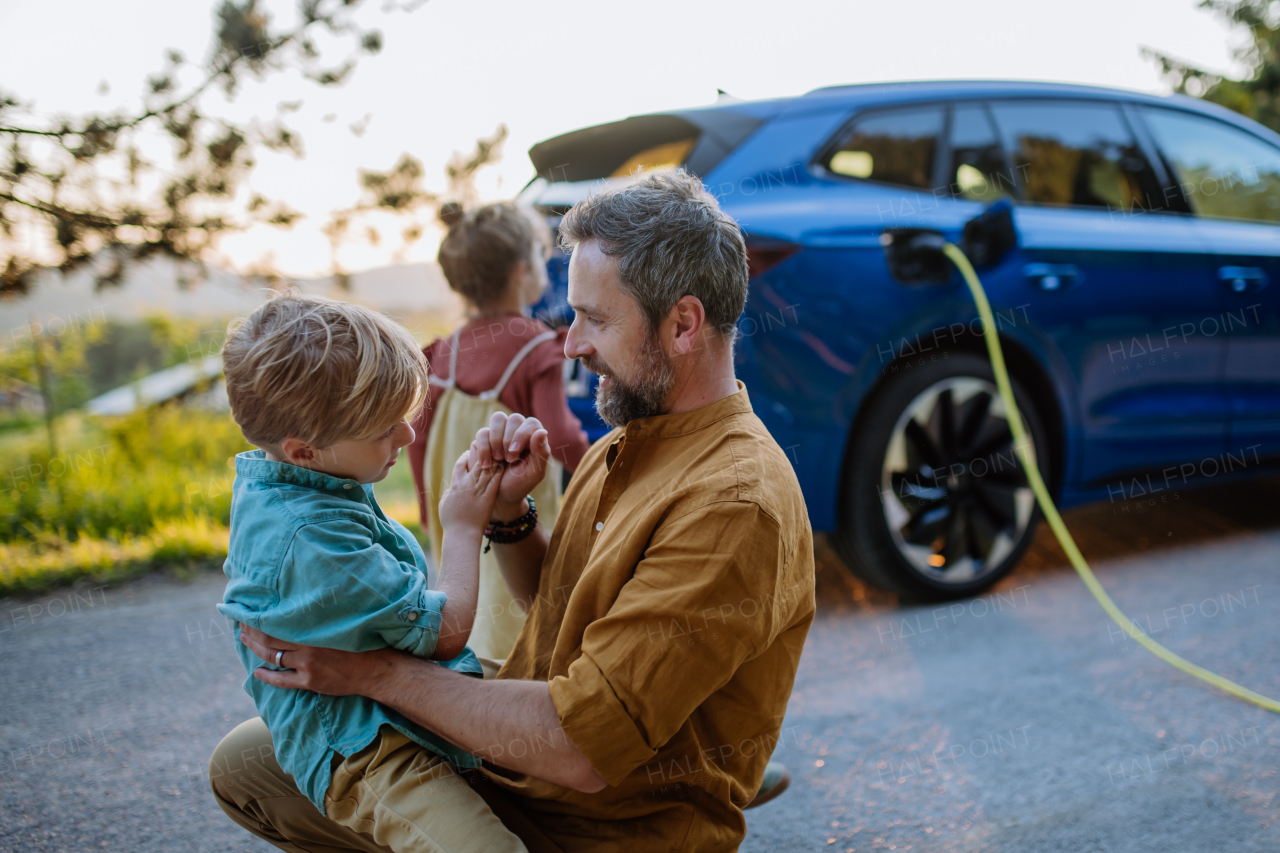 Father with his kids waiting for electric car charging, preparing for trip.