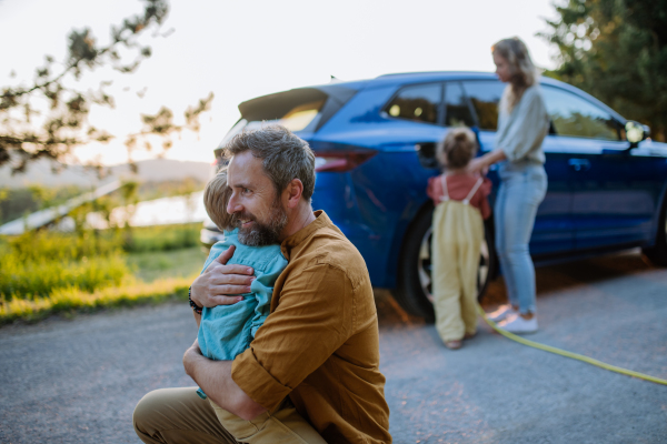 Family with two kids charging their electric car during a family trip.