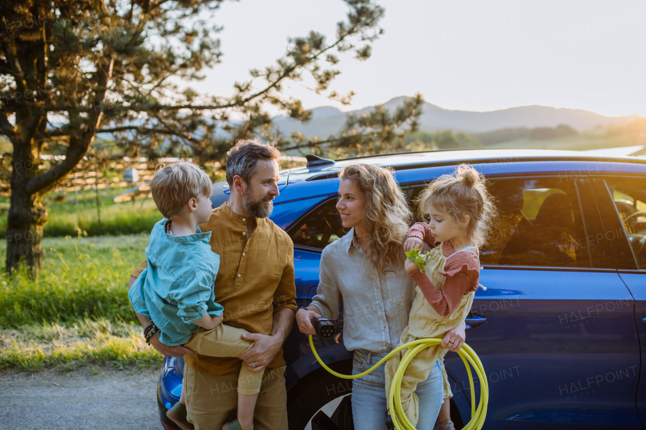 Happy family in front of the electric car, concept of green energy and sustainable lifestyle.