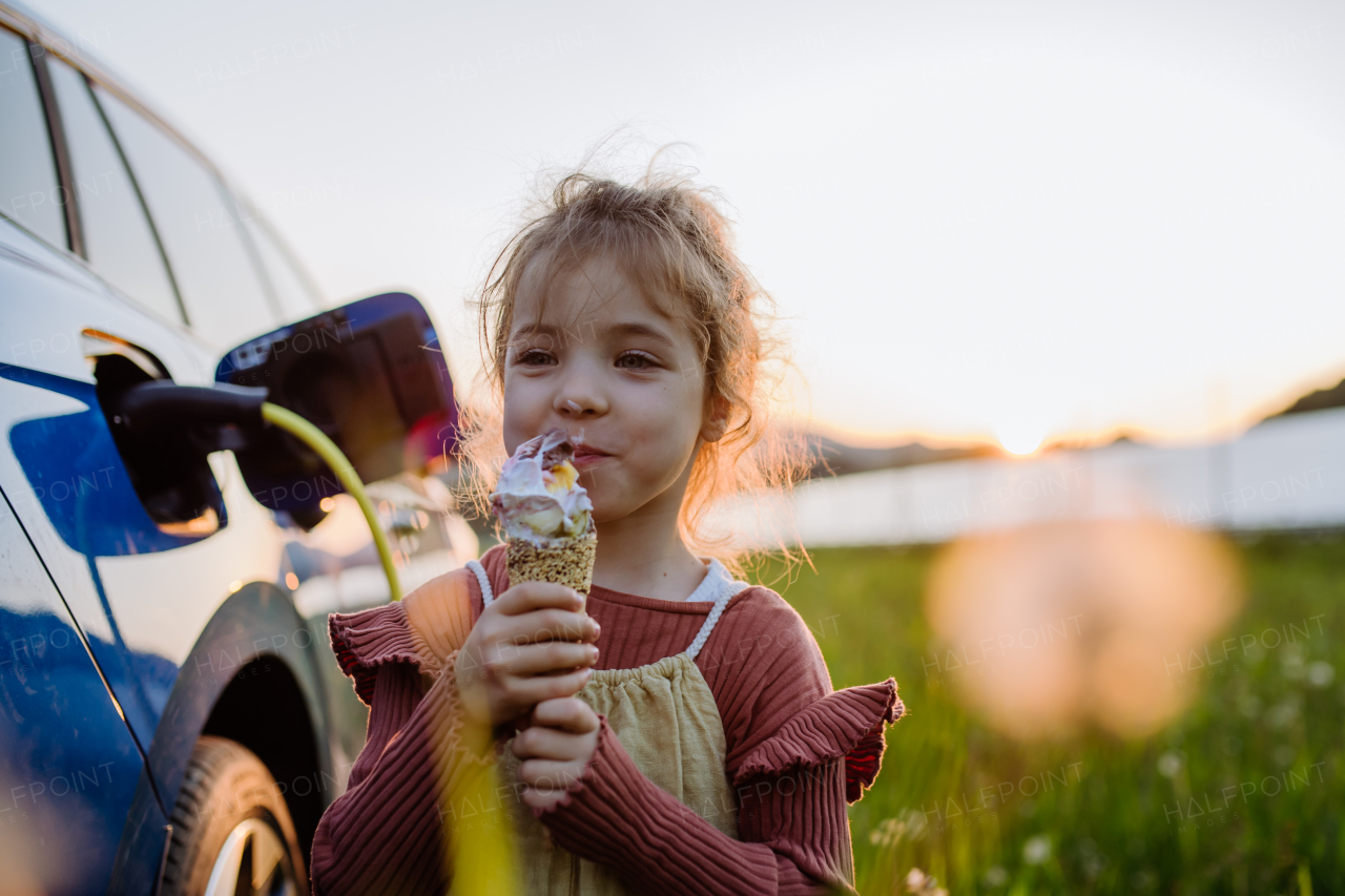 Little girl eating an ice cream while charging their electric car.