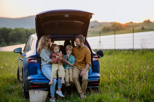 Happy family sitting in a car trunk and waiting for charging, preparationsfor picnic.