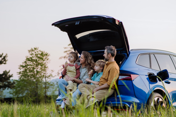 Happy family sitting in a car trunk and waiting for charging, preparationsfor picnic.