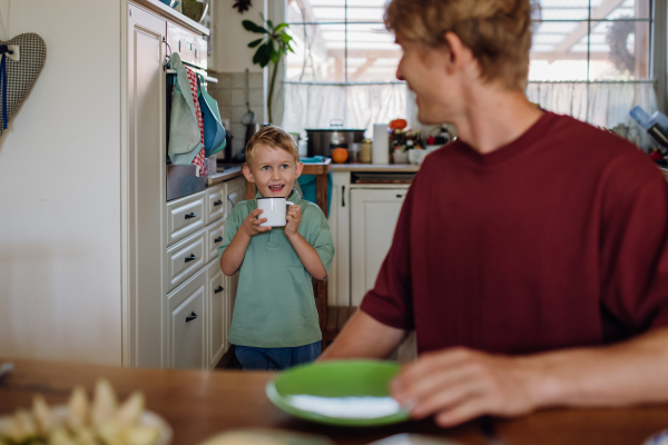 Father and son eating breakfast together in home kitchen. Healthy breakfast or fruit snack before kindergarden.