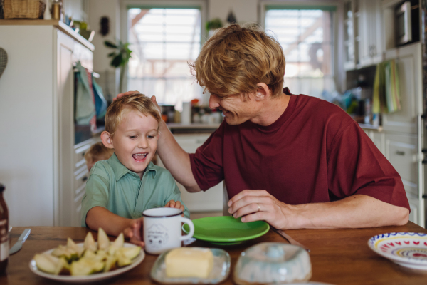 Father and son eating breakfast together in home kitchen. Healthy breakfast or fruit snack before kindergarden.