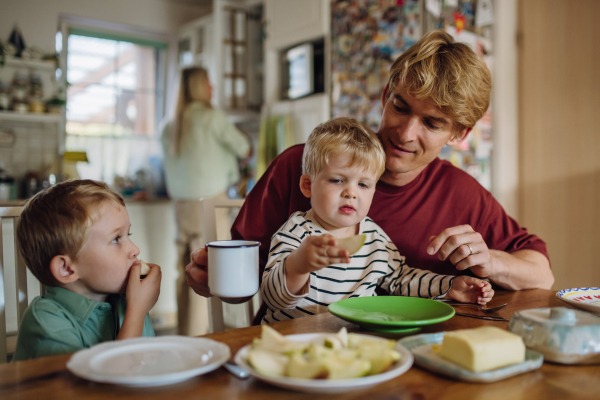 Young family eating breakfast together in home kitchen. Healthy breakfast or snack before kindergarden, school and work.