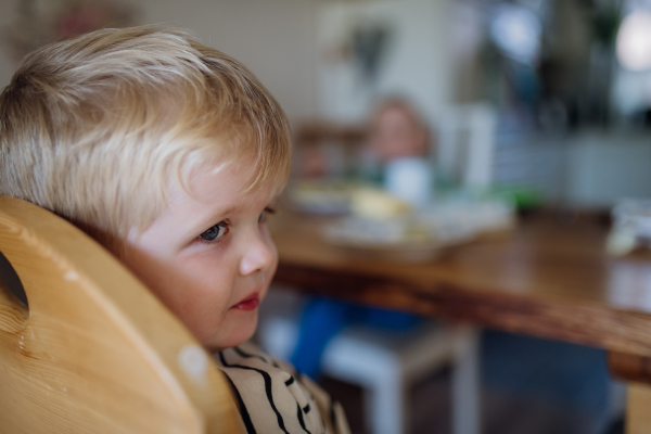 Little cute baby eating breakfast in high chair in home kitchen. Healthy breakfast or snack before day care.