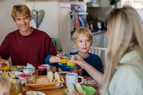 Young family eating breakfast together in home kitchen, toasting with juice. Healty breakfast or snack before school and work.