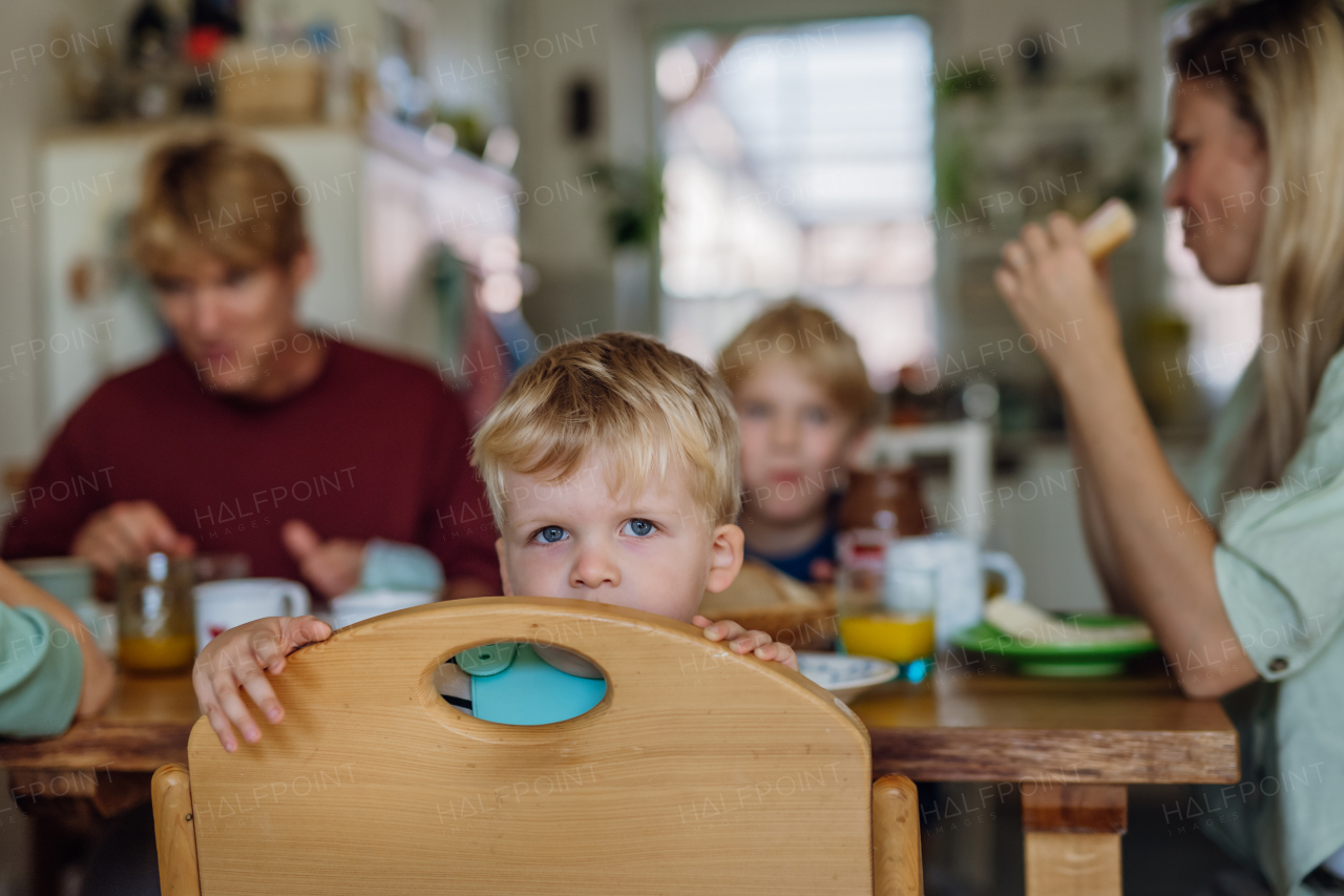 Young family eating breakfast together in home kitchen. Healty breakfast or snack before school and work. Mother helping youngest son.