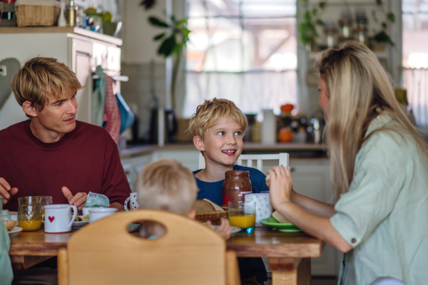 Young family eating breakfast together in home kitchen. Healthy breakfast or snack before kindergarden, school and work.