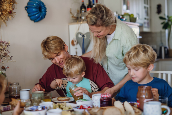 Young family eating breakfast together in home kitchen. Healthy breakfast or snack before kindergarden, school and work.