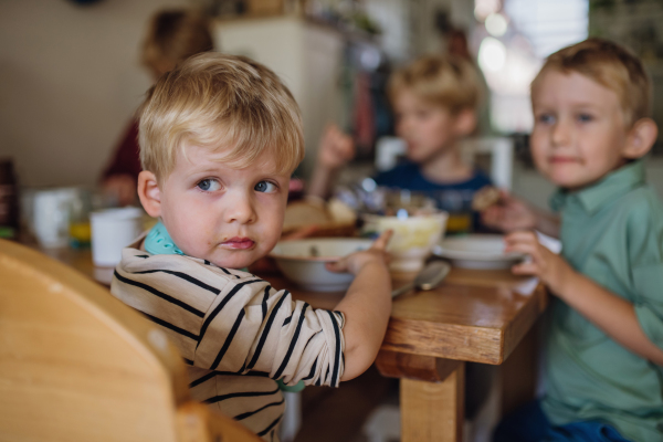 Little cute baby eating breakfast in high chair in home kitchen. Healthy breakfast or snack before day care, preschool.