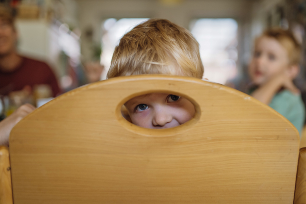 Little boy eating breakfast, looking through hole in the chair. Healthy breakfast or snack before day care.