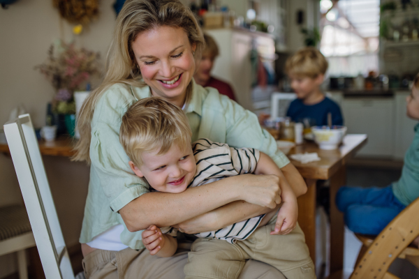 Beautiful mother feeding little baby with breakfast in home kitchen, having fun, laughing.