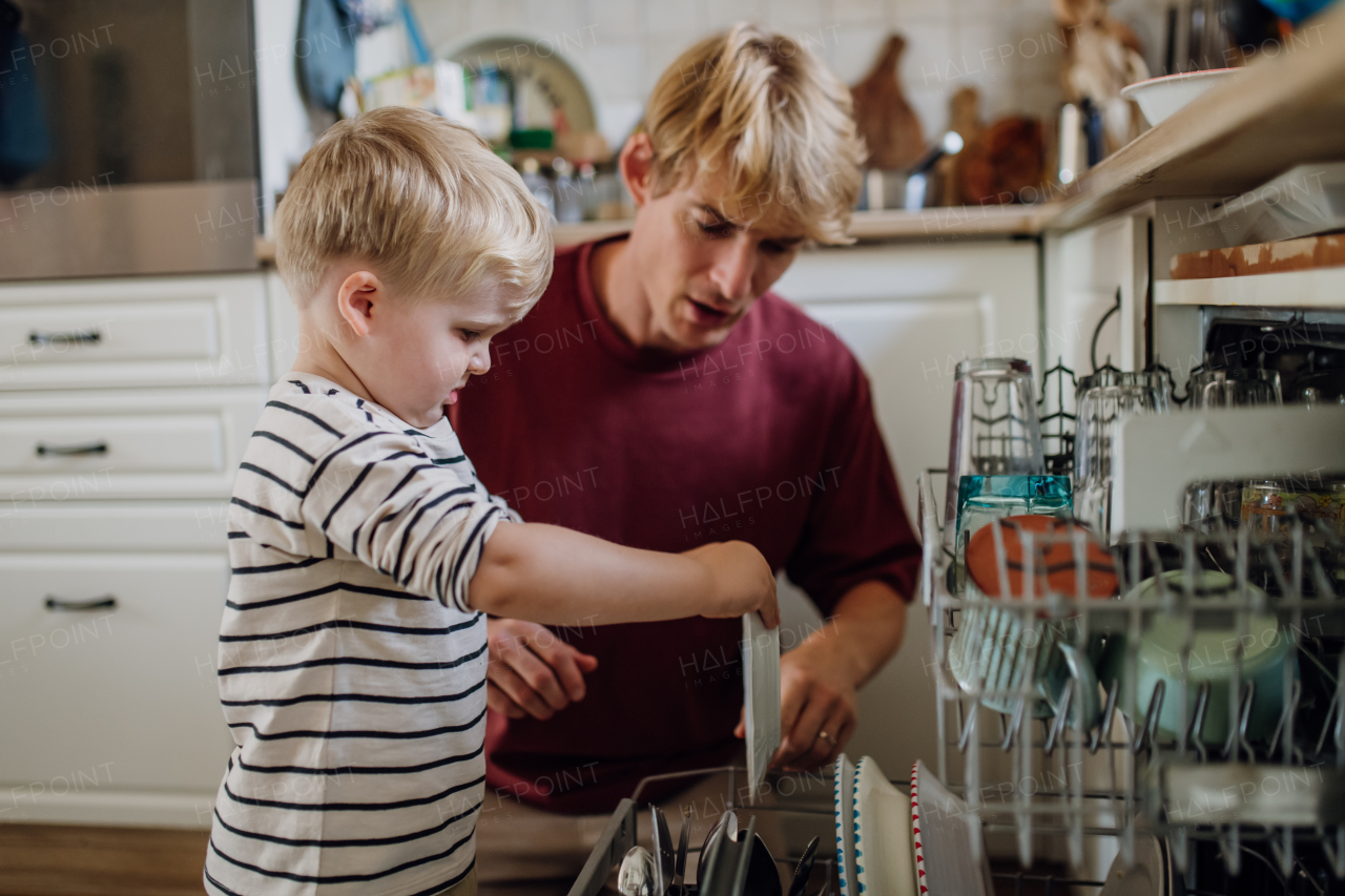 Little boy helping father to load dishwasher after family breakfast. Cleaning kitchen before leaving to work and daycare. Family morning routine.