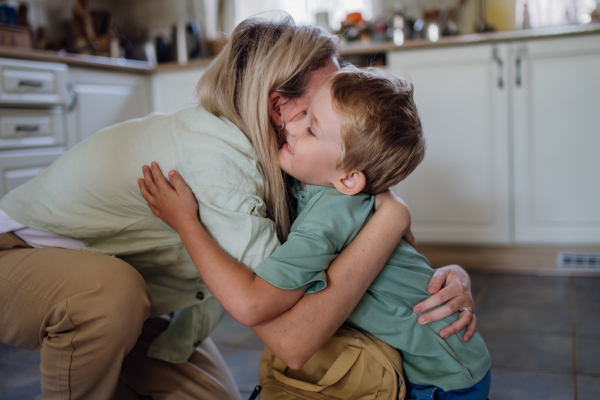 Mother saying goodbyeto to son before school, hugging, embracing him in the kitchen.