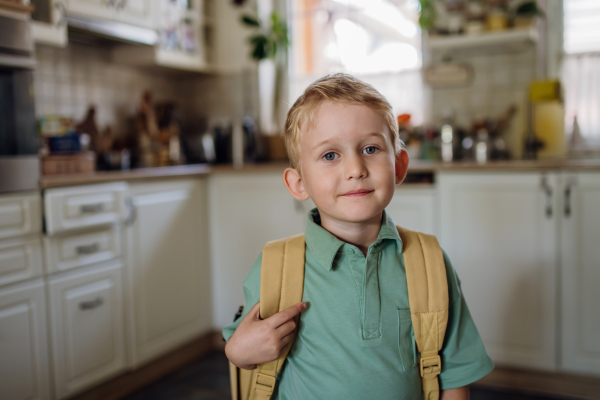 Portrait of schoolboy with backpack on back standing in kitchen. Preparation for school day, morning.