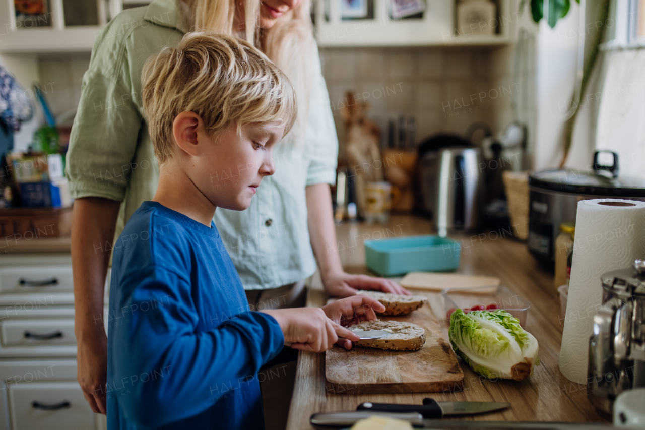 Boy helping mother to make school lunch for lunchbox in the kitchen. Preparing healthy snack for school.