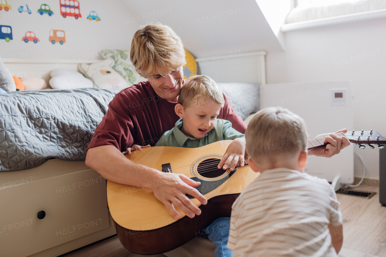 Father teaching boy to play on guitar. Son having fun in their room with dad, playing guitar and singing. Concept of Father's Day, and fatherly love.