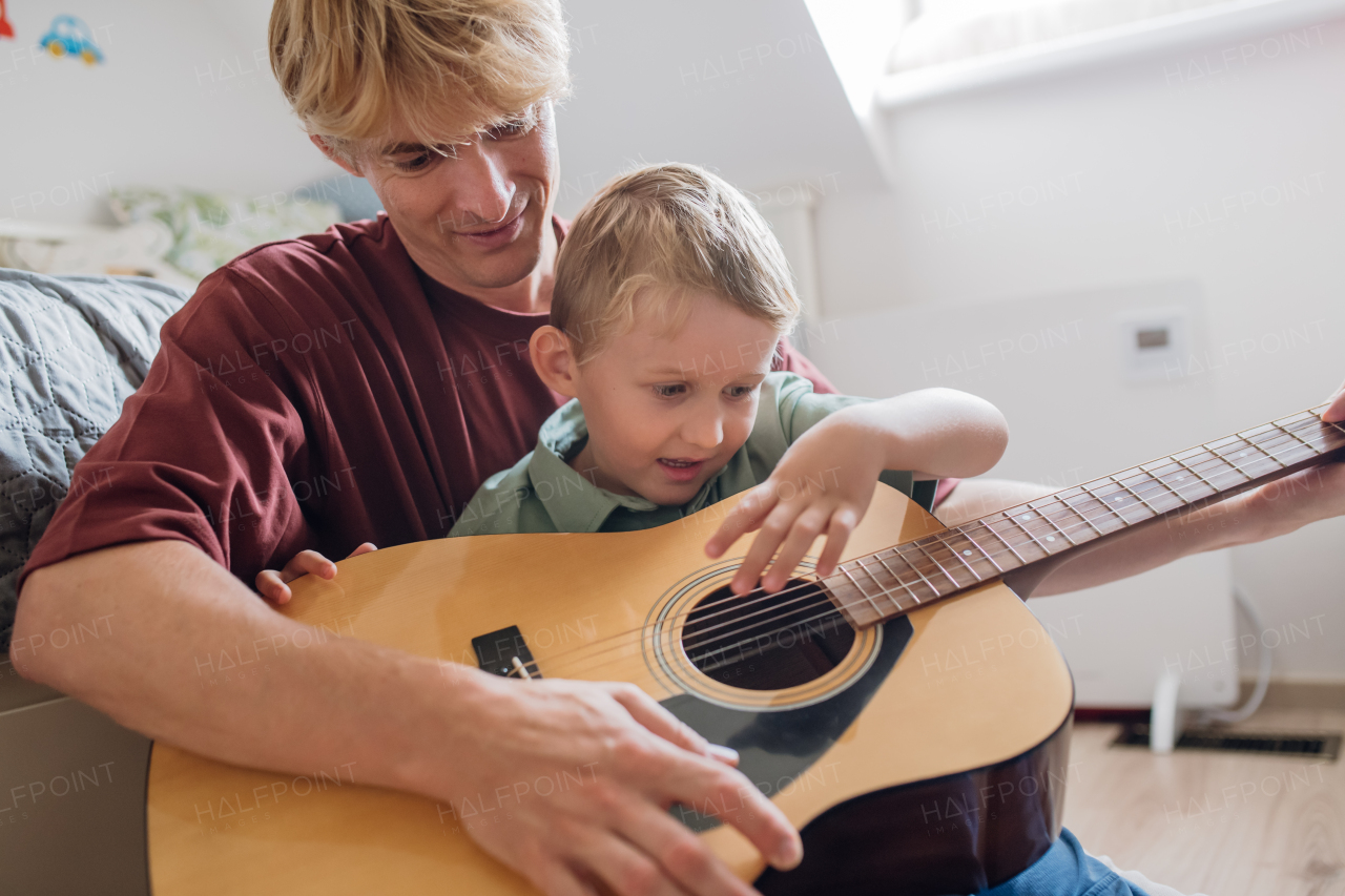 Father teaching boy to play on guitar. Son having fun in their room with dad, playing guitar and singing. Concept of Father's Day, and fatherly love.