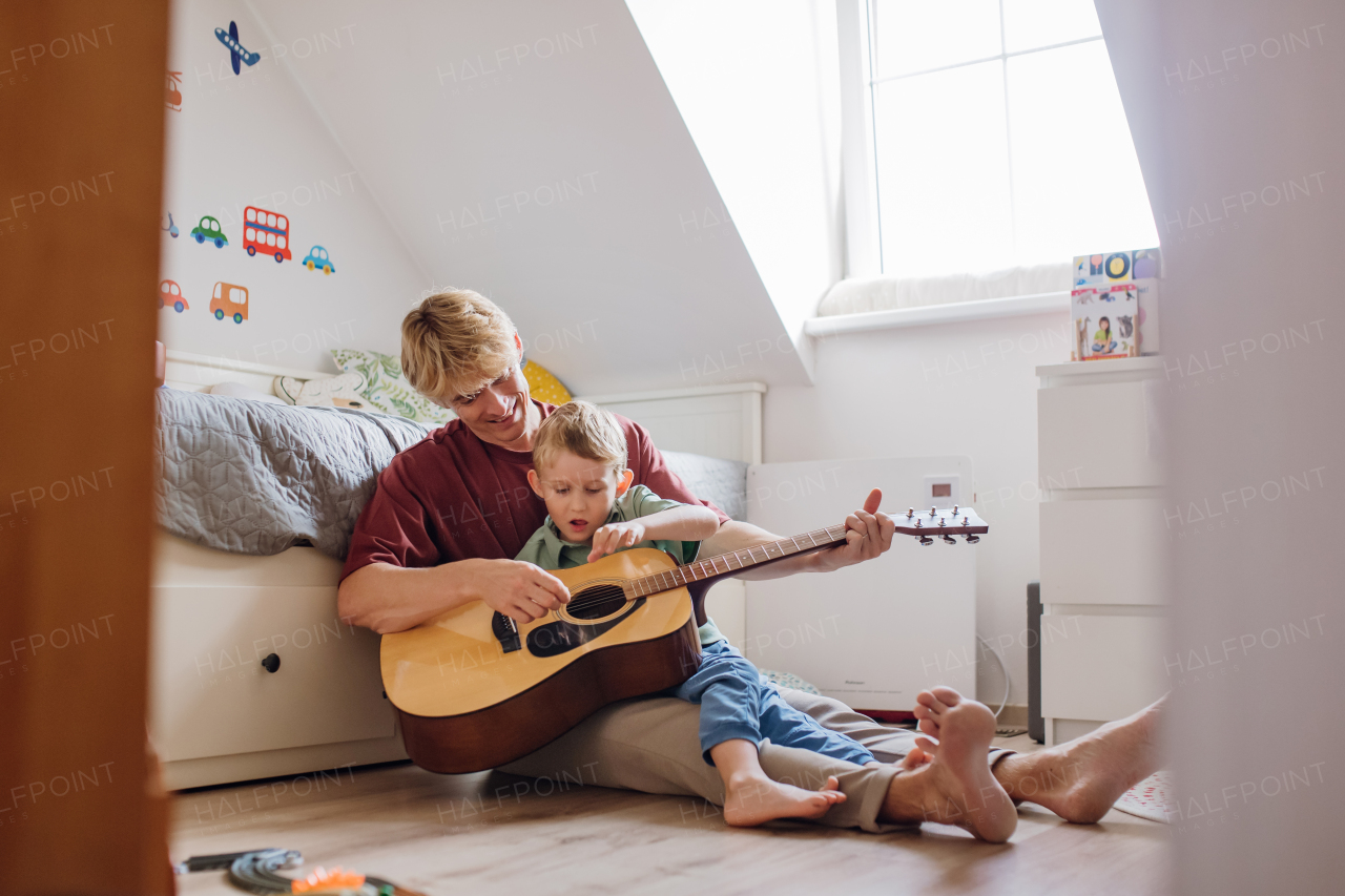 Father teaching boy to play on guitar. Son having fun in their room with dad, playing guitar and singing. Concept of Father's Day, and fatherly love.