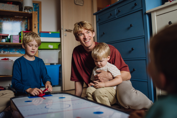 Dad with three sons playing in kids room, air hockey. Concept of Father's Day, and fatherly love. Real family, real people at home.