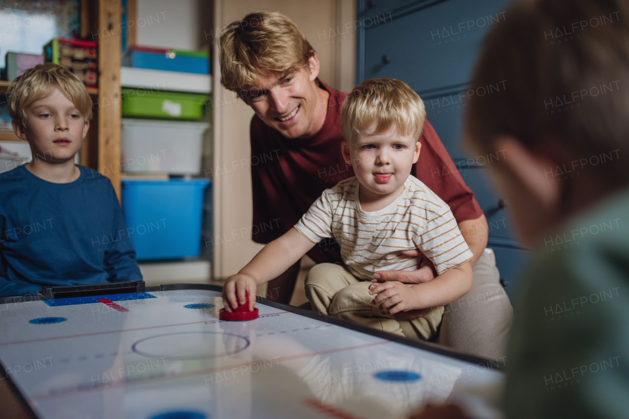 Dad with three sons playing in kids room, air hockey. Concept of Father's Day, and fatherly love. Real family, real people at home.