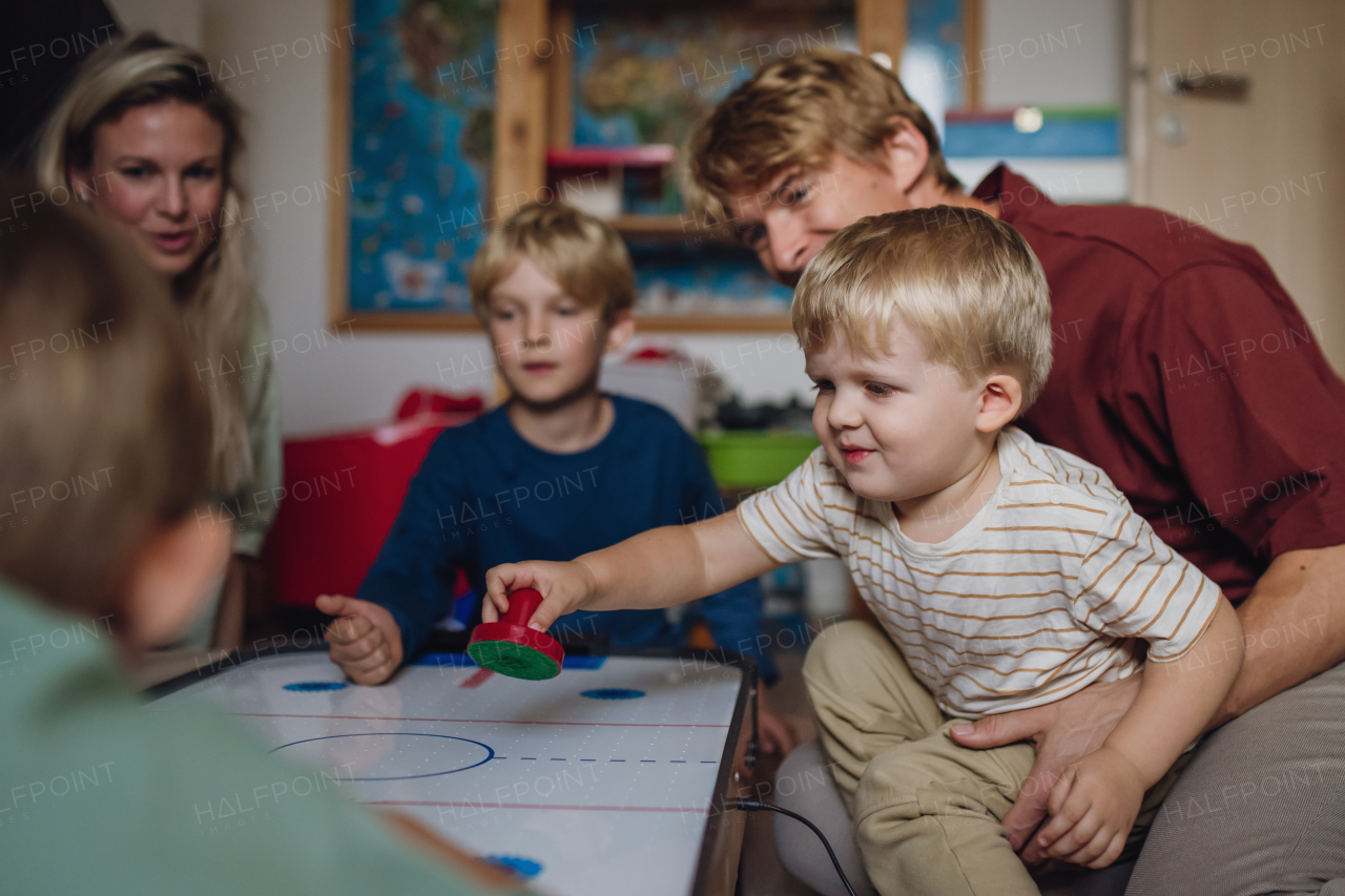 Cheerful family with three kids playing in kids room. Family board game, playtime, having fun together. Air hockey table.