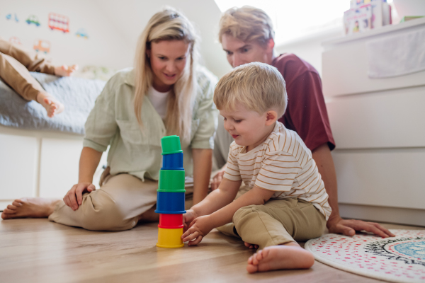 Parents looking at little boy building a tower in childrens room. Stacking blocks, building game for the preschooler.