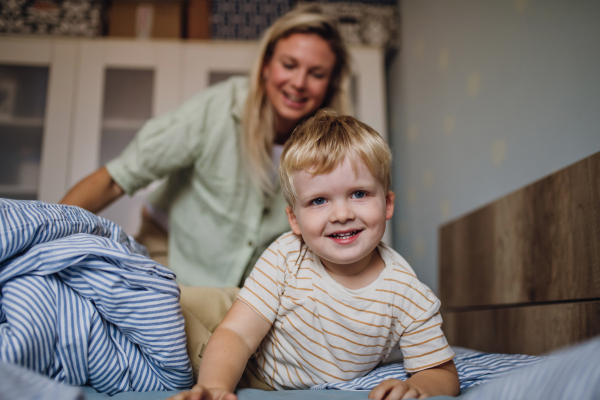 Portrait of cute little baby boy waking up in the morning. Mother helping son out of bed.