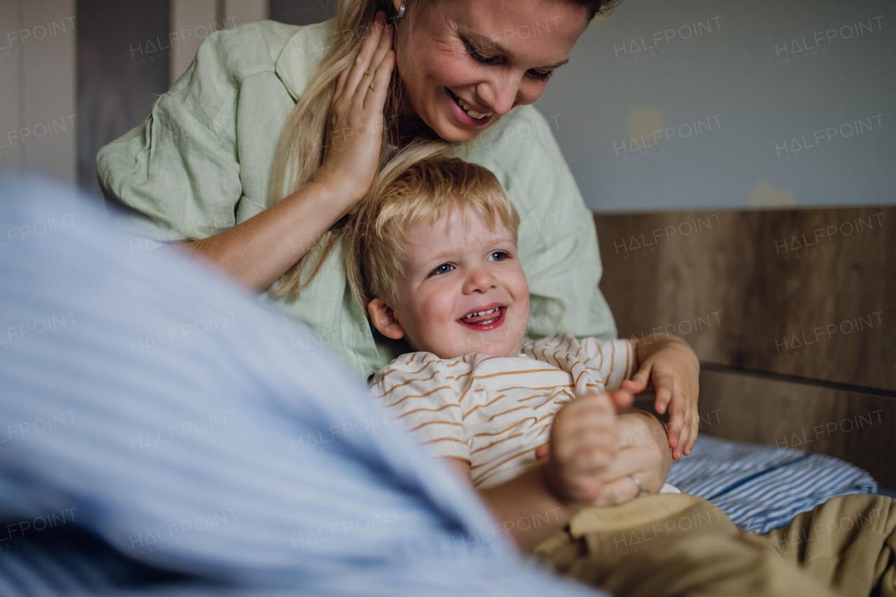 Portrait of cute little baby boy waking up in the morning. Mother helping son out of bed.