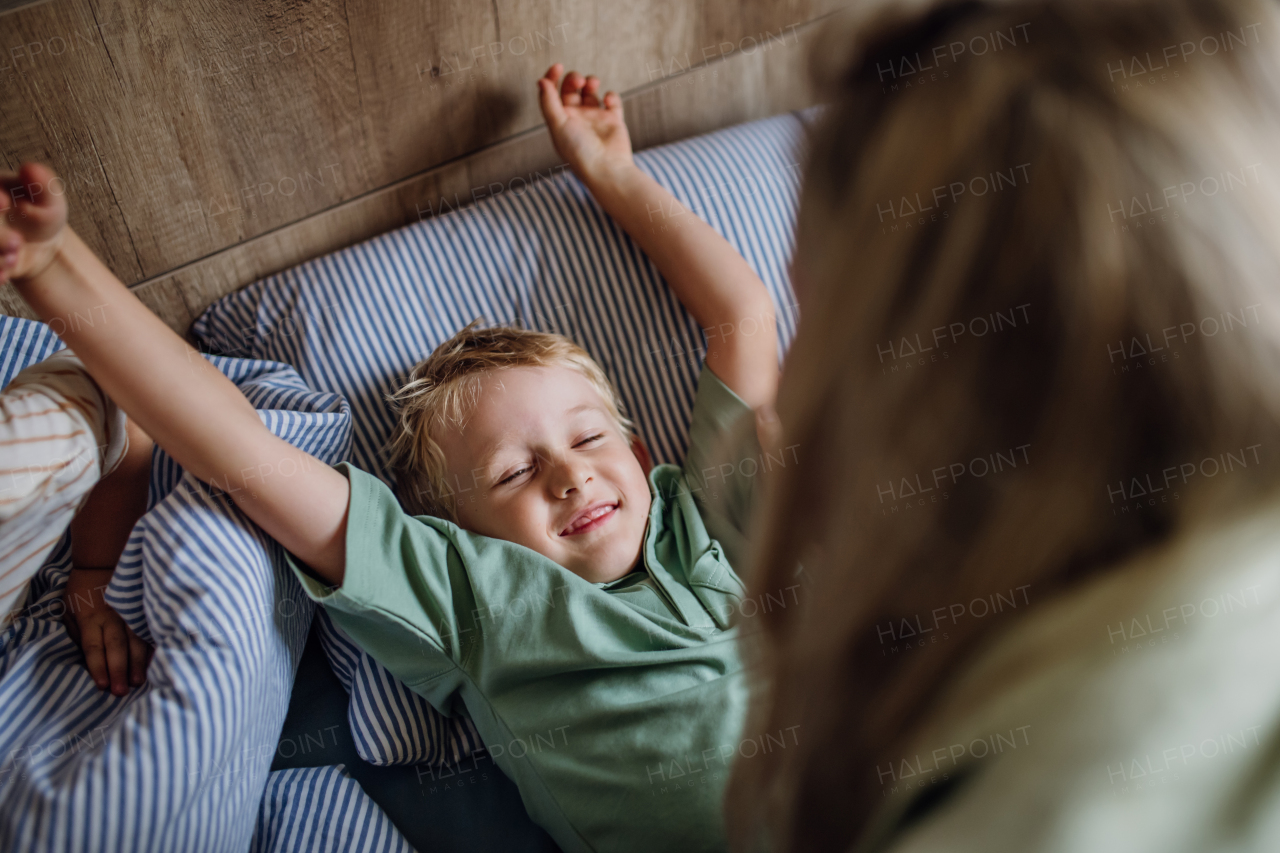 Young boy waking up in the morning for the school. Mother helping son out of bed, preparing him for first day at school.