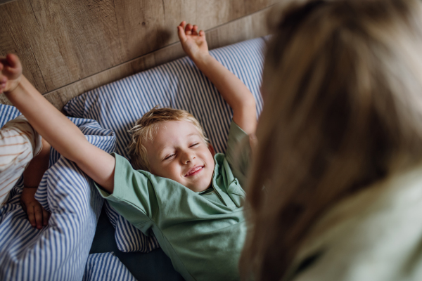 Young boy waking up in the morning for the school. Mother helping son out of bed, preparing him for first day at school.