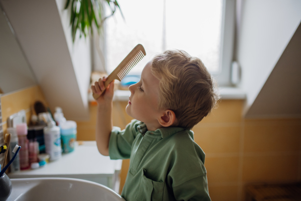 Schoolboy combing his hair in the morning before going to school. Morning routine for schoolkids.