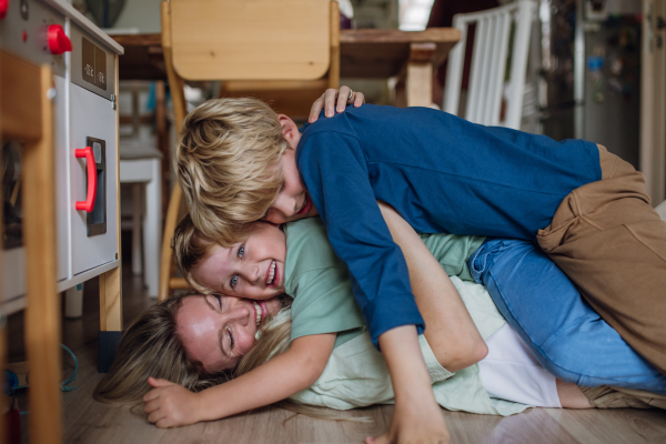 Portrait of mom having fun with sons, lying on each other floor in living room. Beautiful mother with her two sons looking the camera and laughing.