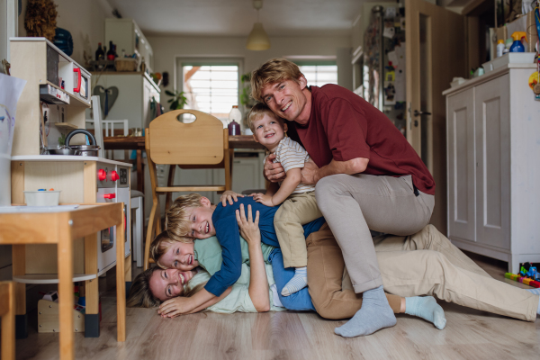 Portrait of family having fun, sitting, lying on each other floor in living room. Beautiful mother with her three sons and husband looking the camera and laughing.