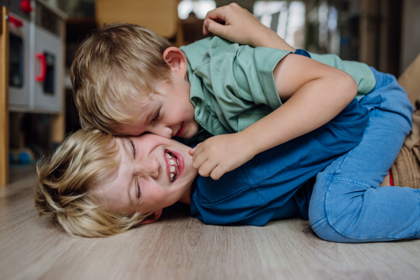 Two little boys fighting and lying on the floor, brothers having fun at home. Concept of sibling relationship and brotherly love.