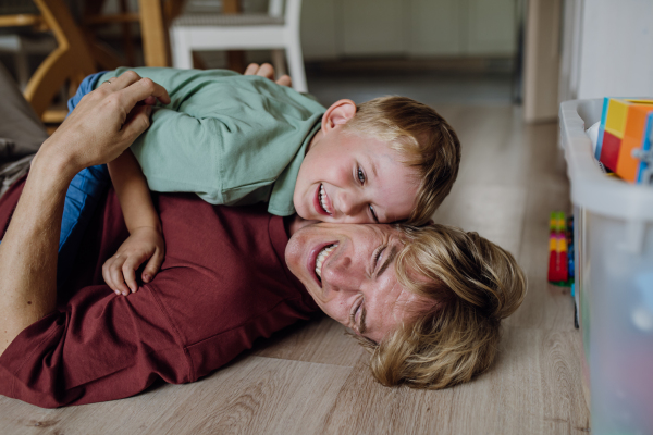 Portrait of father embracing his son at home, having fun, lying on floor and laughing. Dad and boy spending quality time together, bonding.