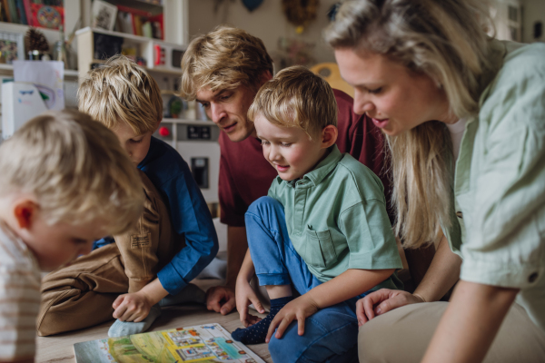 Cheerful family with three kids reading book in living room, on floor, having fun together.