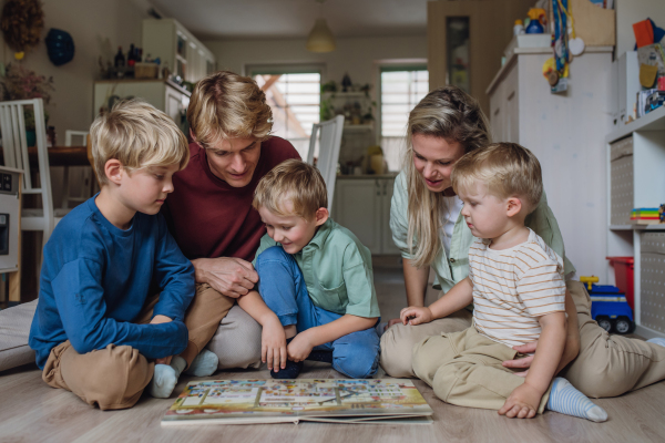 Cheerful family with three kids reading book in living room, on floor, having fun together.