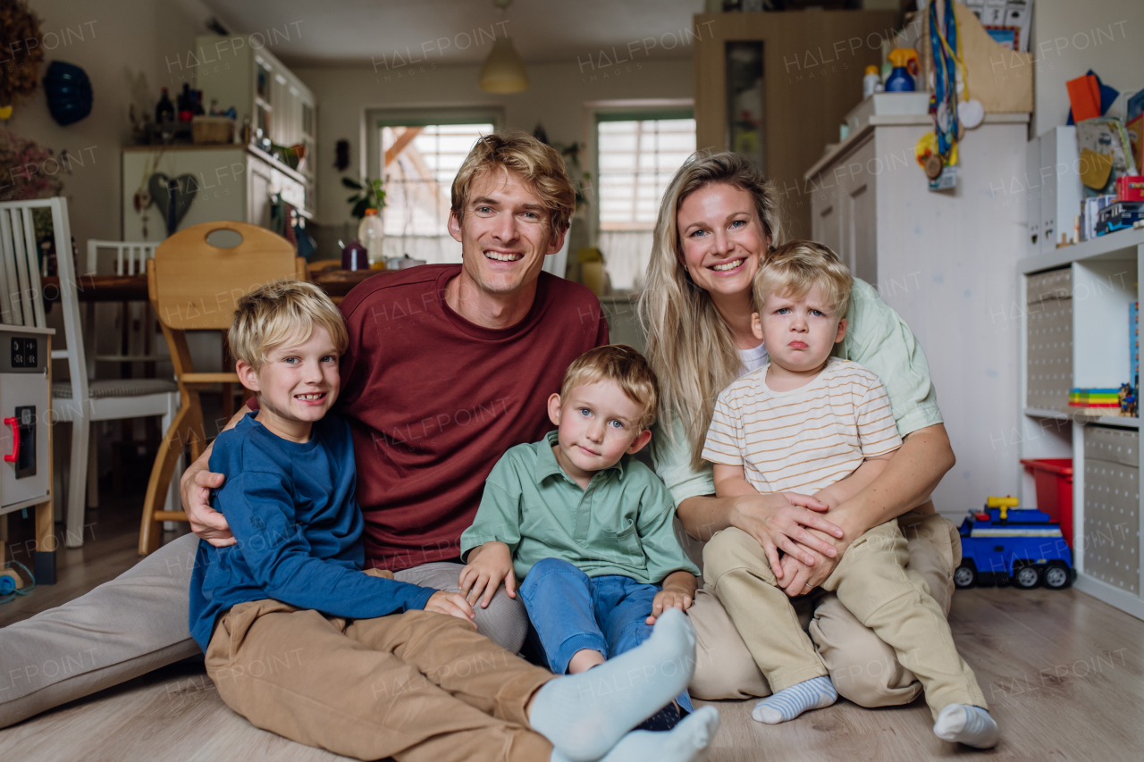 Portrait of young family at home siting on the floor. Beautiful mother with her three sons and husband in the living room.