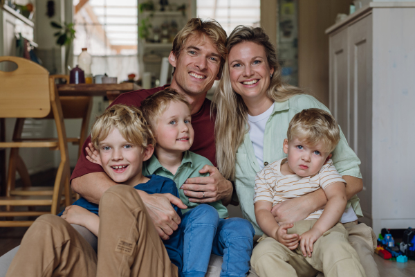 Portrait of family sitting on floor in living room. Beautiful mother with her three sons and husband looking the camera and smiling.