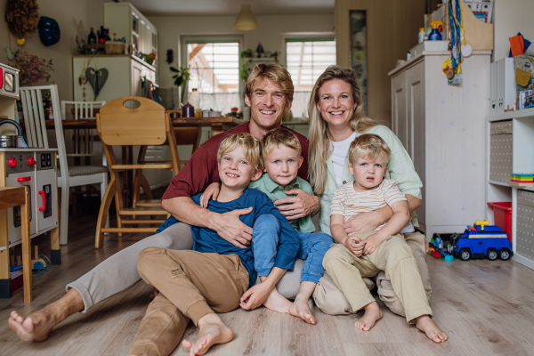 Portrait of family sitting on floor in living room. Beautiful mother with her three sons and husband looking the camera and smiling.