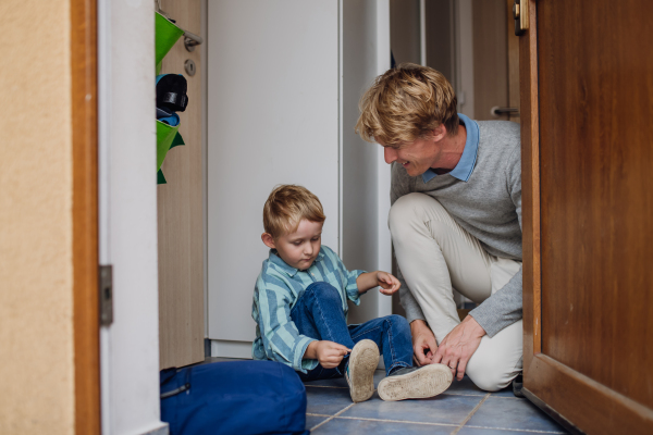 Boy getting ready for school, putting on the shoes, getting dressed. Father taking son to school before going to work.