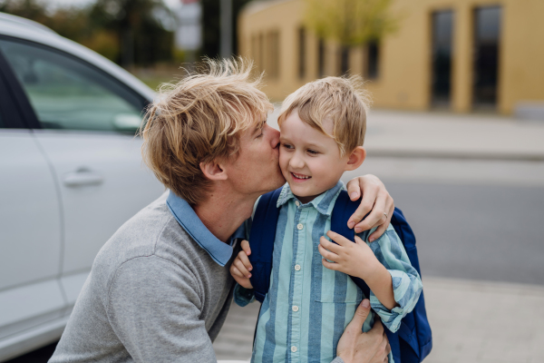 Father saying goodbyeto to son in front of school building, hugging and kissing him on the cheek. Dad heading to work. Concept of work-life balance for parents.