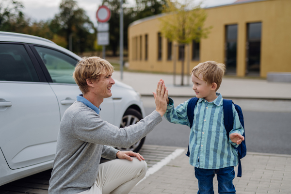 Father saying goodbyeto to his son in front of school building, high five each other. Dad heading to work. Concept of work-life balance for parents.